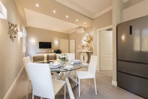 A modern kitchen with a stainless steel refrigerator, a dining area with a glass table and white chairs, and a flat-screen TV mounted on the wall. - Michelangelo Hideaway (Florence)
