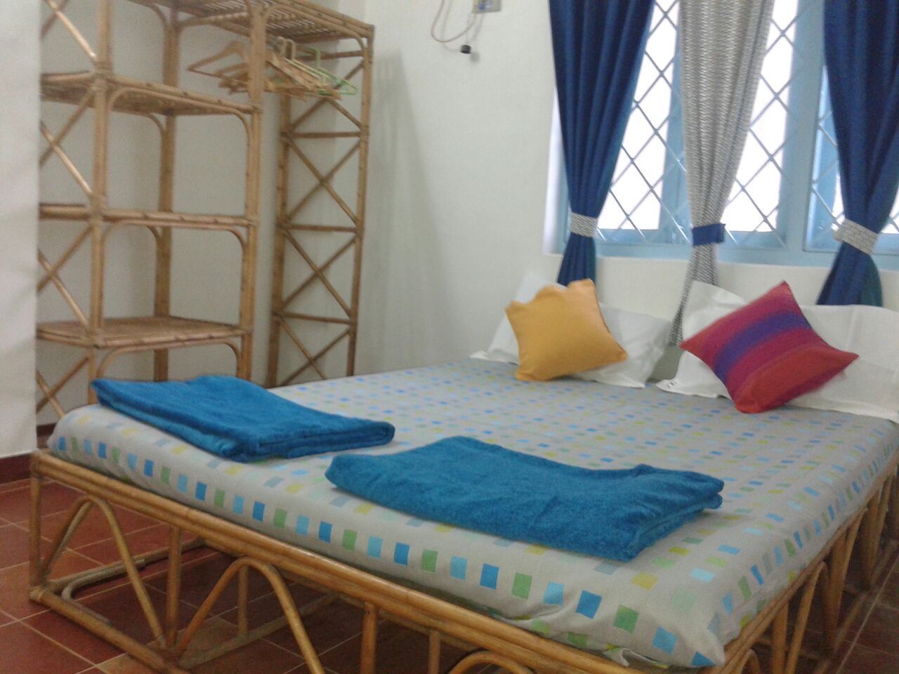 A room with a bed, a wicker chair, and a window with curtains.