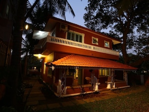 A two-story building with a covered porch and a pathway leading to the entrance. - Joshua's Beach House | 6 BHK AC Villa Near Calangute Beach, Goa (Calangute)