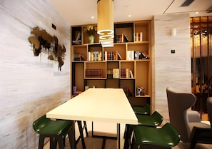 A modern conference room with a long table, green chairs, and a bookshelf filled with books. - City Comfort Inn Changzhou Global Harbor Dinosaur Park (Changzhou)