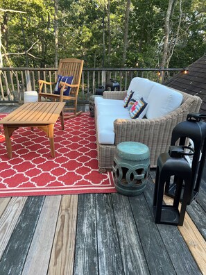 A wooden deck with a wicker sofa, a rocking chair, and a small table.