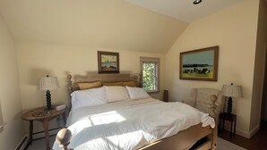 A bedroom with a large bed, two bedside tables, a chair, and two paintings on the walls. - Fabulous 3-bedroom house in Biddeford perfect for your beach getaway (Biddeford)