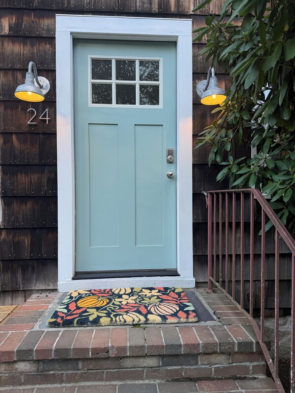 A light blue door with a numerical address sign, a doormat, and two wall-mounted lights.