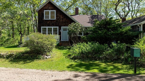 A wooden cabin with a gabled roof, surrounded by dense greenery and a stone wall. - Fabulous 3-bedroom house in Biddeford perfect for your beach getaway (Biddeford)
