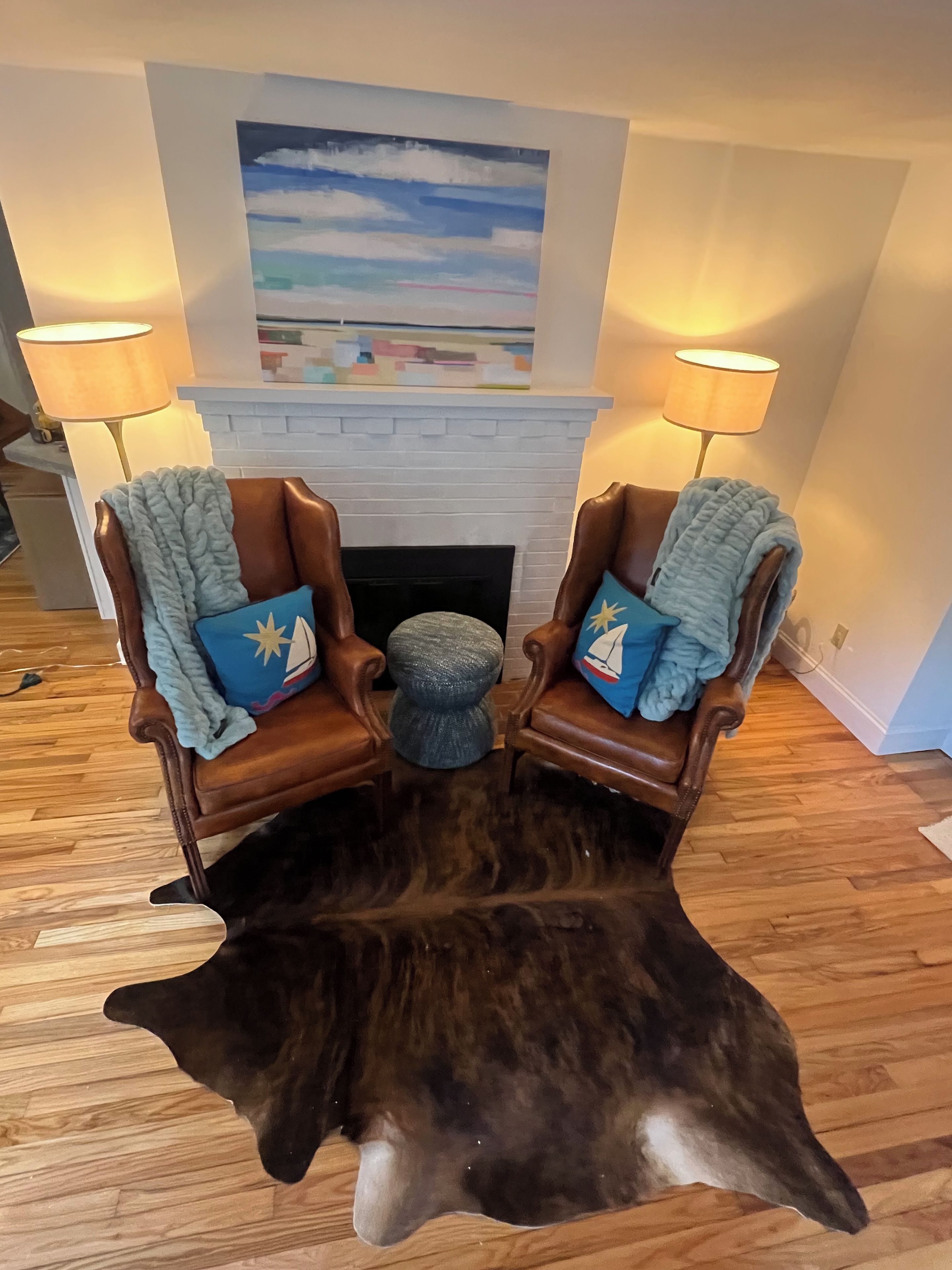 Une pièce avec une cheminée, deux fauteuils en cuir accompagnés de plaids, un tapis et une grande peau d’animal sur le sol.
