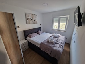 Un dormitorio con cama, mesitas de noche, una ventana con persianas y un cuadro en la pared.
