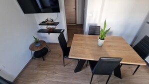 Ein moderner Essbereich mit einem Holztisch, schwarzen Stühlen, einer Topfpflanze und einem an der Wand befestigten Fernseher.