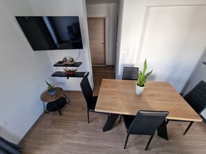 Un'area pranzo moderna con un tavolo di legno, sedie nere, una pianta in vaso e un televisore fissato al muro.