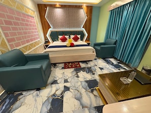 A hotel room with a bed, two armchairs, a coffee table, a patterned floor, and a curtain. - F.M, (Kanthi)