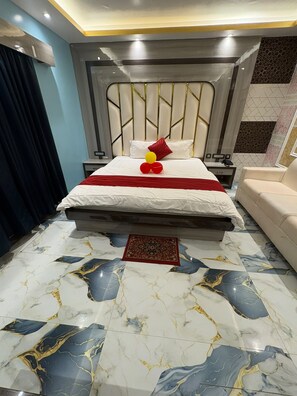 A hotel room with a bed, bedside tables, a sofa, and a patterned rug. - F.M, (Kanthi)