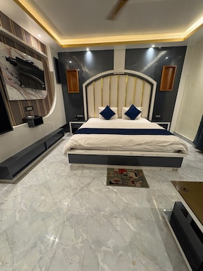 A modern bedroom with a large bed, a TV mounted on the wall, and a marble floor. - F.M, (Kanthi)