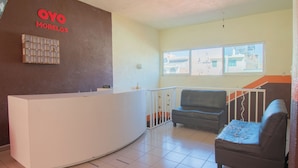 Un área de recepción con un mostrador blanco, un sofá de cuero negro y vistas a edificios a través de una ventana.