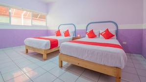 Dos camas individuales con cabeceros de madera y ropa blanca, almohadas rojas y una mesita con un cartel entre ellas.