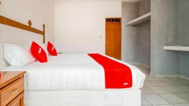 Habitación con cama individual, cabecera de madera, colchón blanco y detalles en rojo.