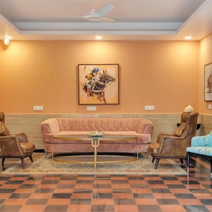 Una habitación con piso a cuadros, un sofá rosa, dos sillones de cuero, una mesa de centro de vidrio y un ventilador de techo.