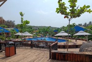 Una terraza de madera con piscina, rodeada de sombrillas y sillones de descanso.