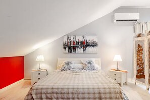 Un dormitorio con una cama, dos mesitas de noche, un mueble auxiliar, un equipo de aire acondicionado y un adorno en la pared.