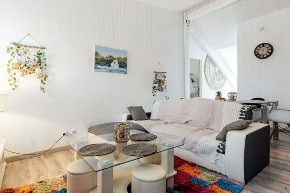 Una sala moderna con una mesa de centro de cristal, sofá blanco y alfombra colorida.