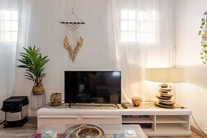 Una sala de estar con un televisor de pantalla plana, un mueble blanco para equipo audiovisual, una lámpara y una planta.