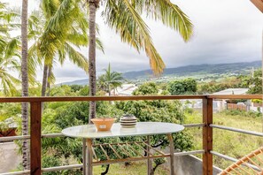 Un balcón con mesa, barandilla y vista a un paisaje de palmeras y colinas distantes.