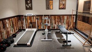 Academia com equipamentos de ginástica, um banco e espelho fixado na parede.