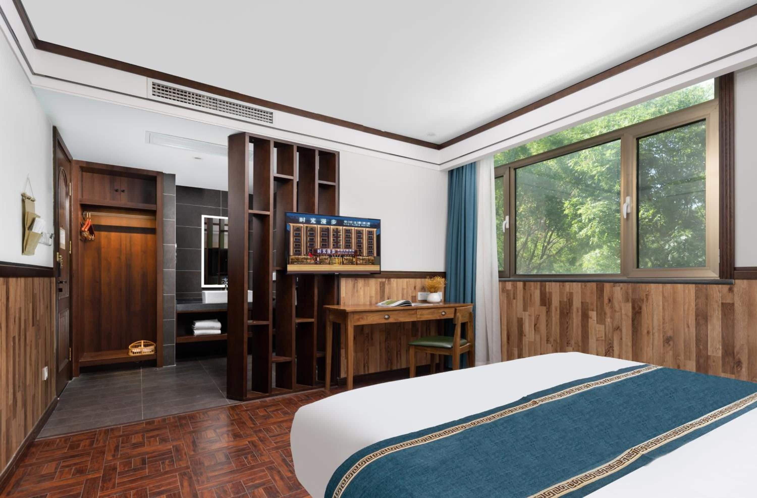 A hotel room with a bed, a desk, a chair, a window, and a view of trees.