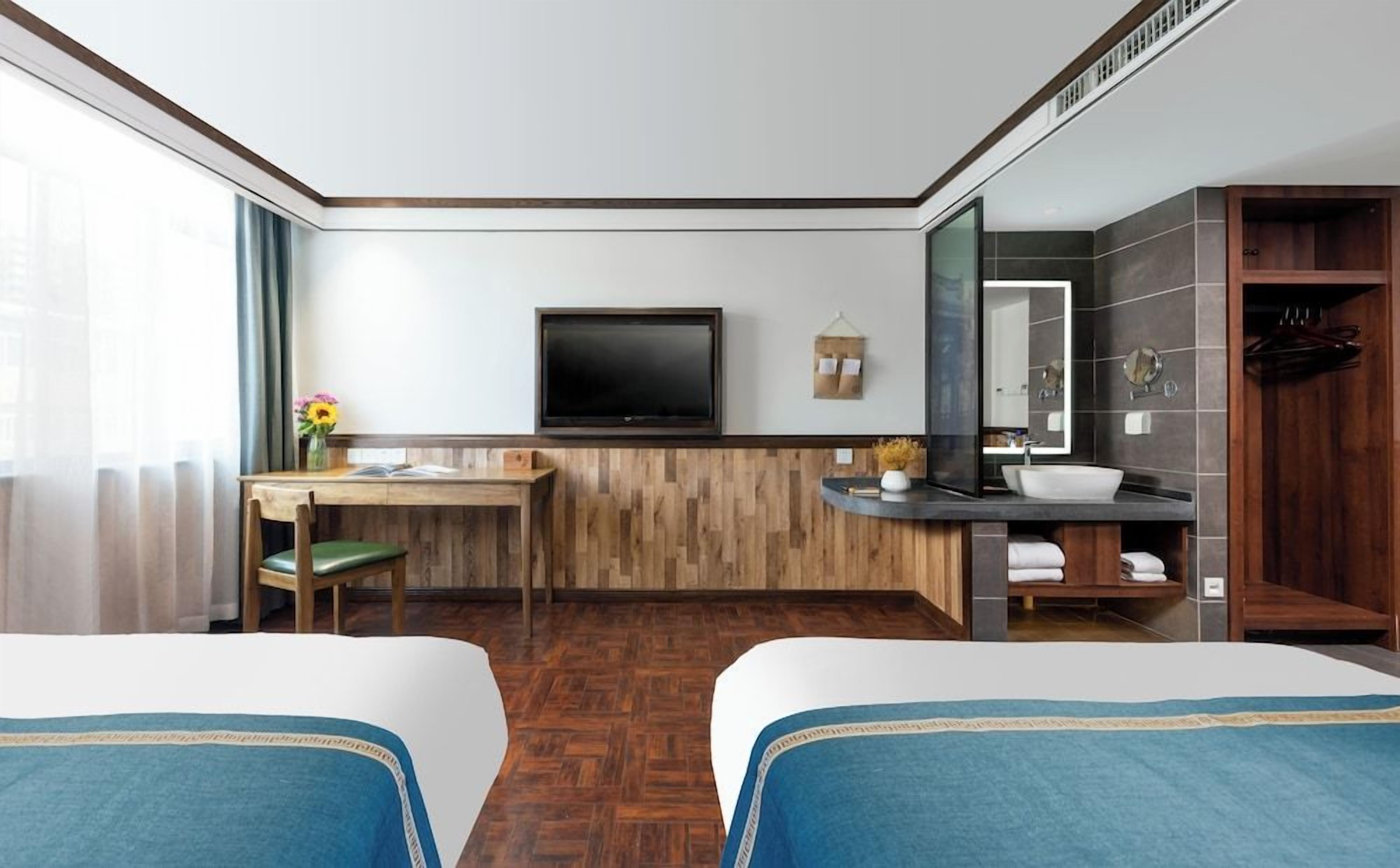 Habitación de hotel con dos camas, un escritorio, un televisor, un baño con lavamanos y espejo, y vista al exterior.