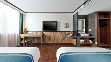 Habitación de hotel con dos camas, un escritorio, un televisor, un baño con lavamanos y espejo, y vista al exterior.