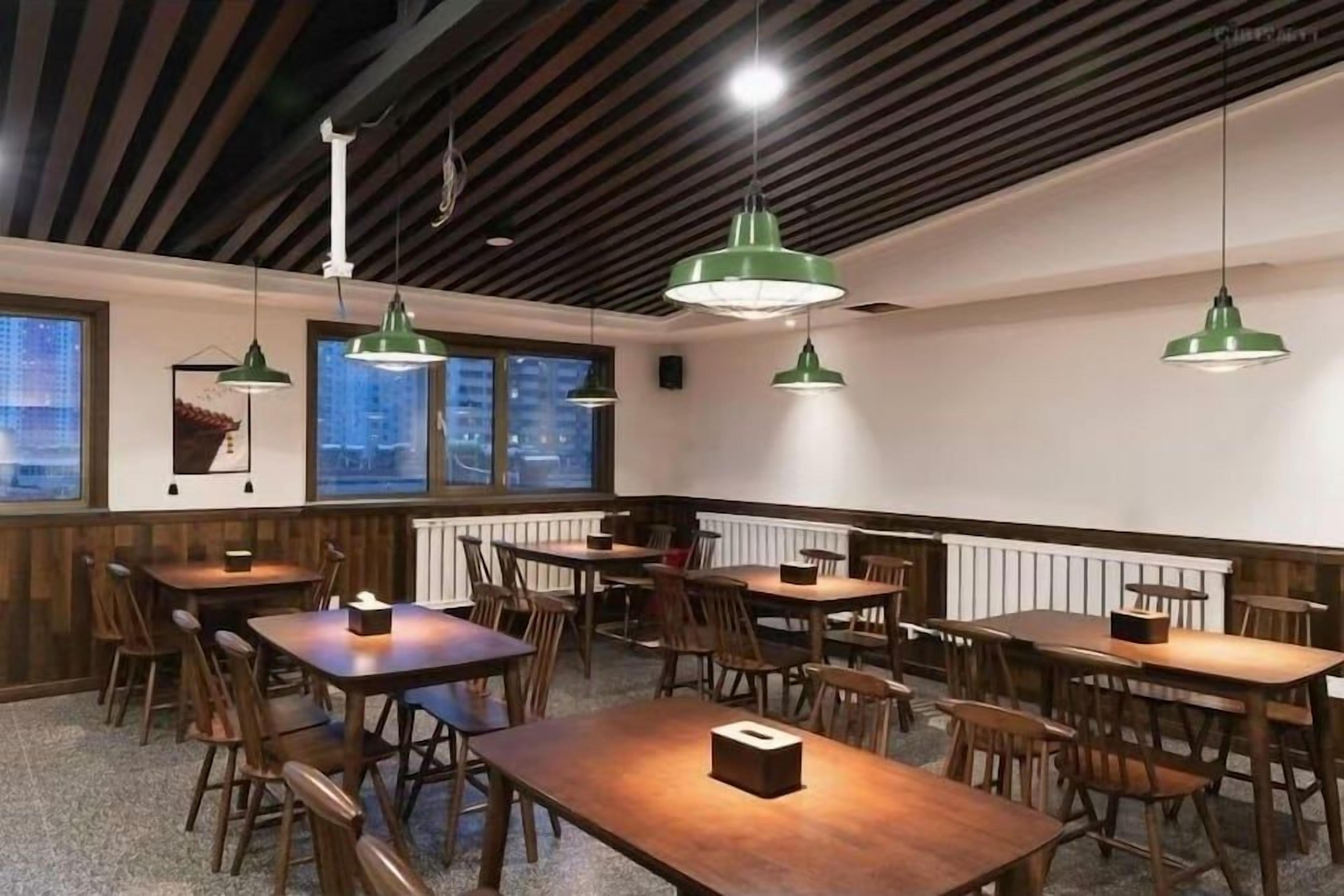 Un comedor con mesas y sillas de madera, luces colgantes y vistas a través de las ventanas.