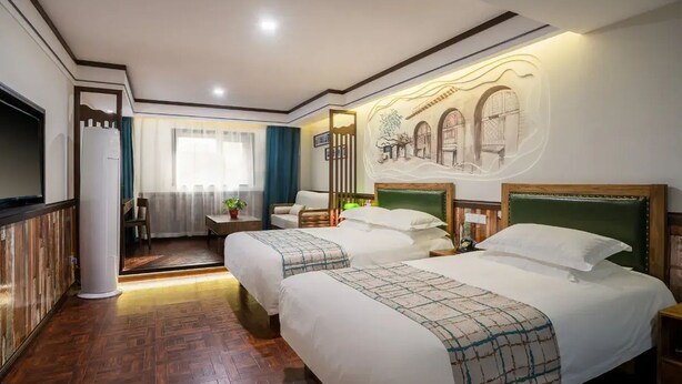Quarto de hotel com duas camas, piso de madeira, uma janela grande com cortinas e um mural na parede.