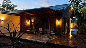 A modern outdoor patio with a wooden deck, a dining area with chairs and a table, and a small blue bathtub. - Together Lifestyle Resort (Thulamela)
