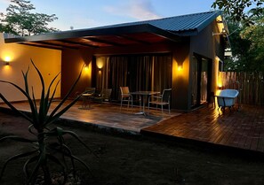 A modern outdoor patio with a wooden deck, a dining area with chairs and a table, and a small blue bathtub. - Together Lifestyle Resort (Thulamela)