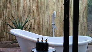 A white bathtub with a faucet, a small stool with three bottles, and a bamboo fence in the background. - Together Lifestyle Resort (Thulamela)