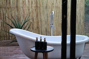 A white bathtub with a faucet, a small stool with three bottles, and a bamboo fence in the background. - Together Lifestyle Resort (Thulamela)