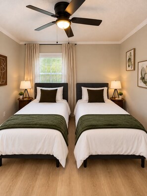 Ein Hotelzimmer mit zwei Betten, einem Deckenventilator, einem Fenster mit Vorhängen und Wandlampen.