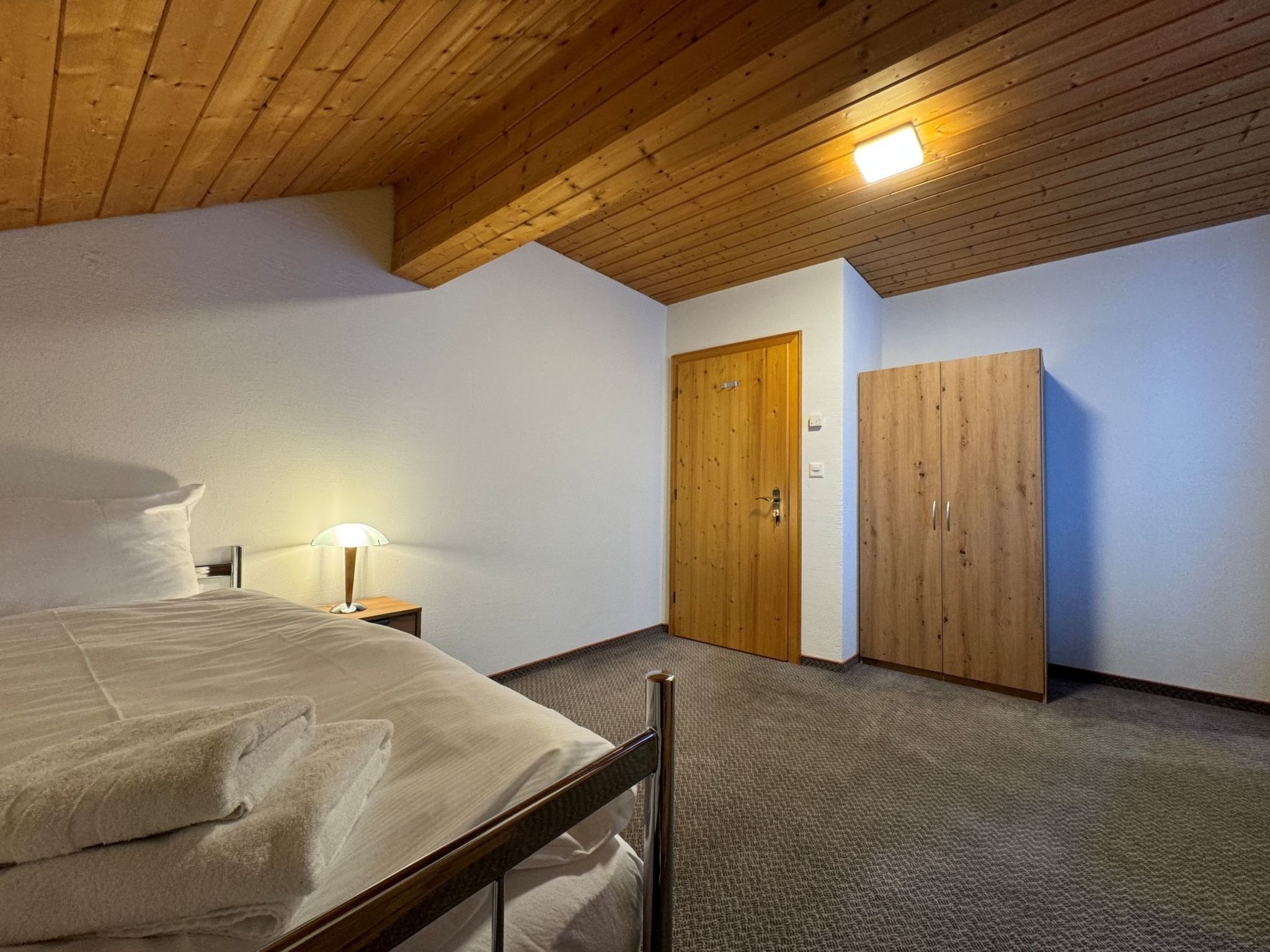 Une chambre à coucher avec un lit, une table de chevet, une lampe, une armoire et une porte.