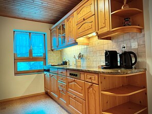 Eine Küche mit Holzschränken, einem fenster mit Vorhängen, einer Kaffeemaschine und einer gefliesten Spritzschutzwand.