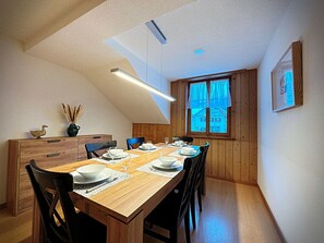 Ein Essbereich mit Holztisch für vier Personen, einem Holzschrank und einem Fenster mit Vorhängen.
