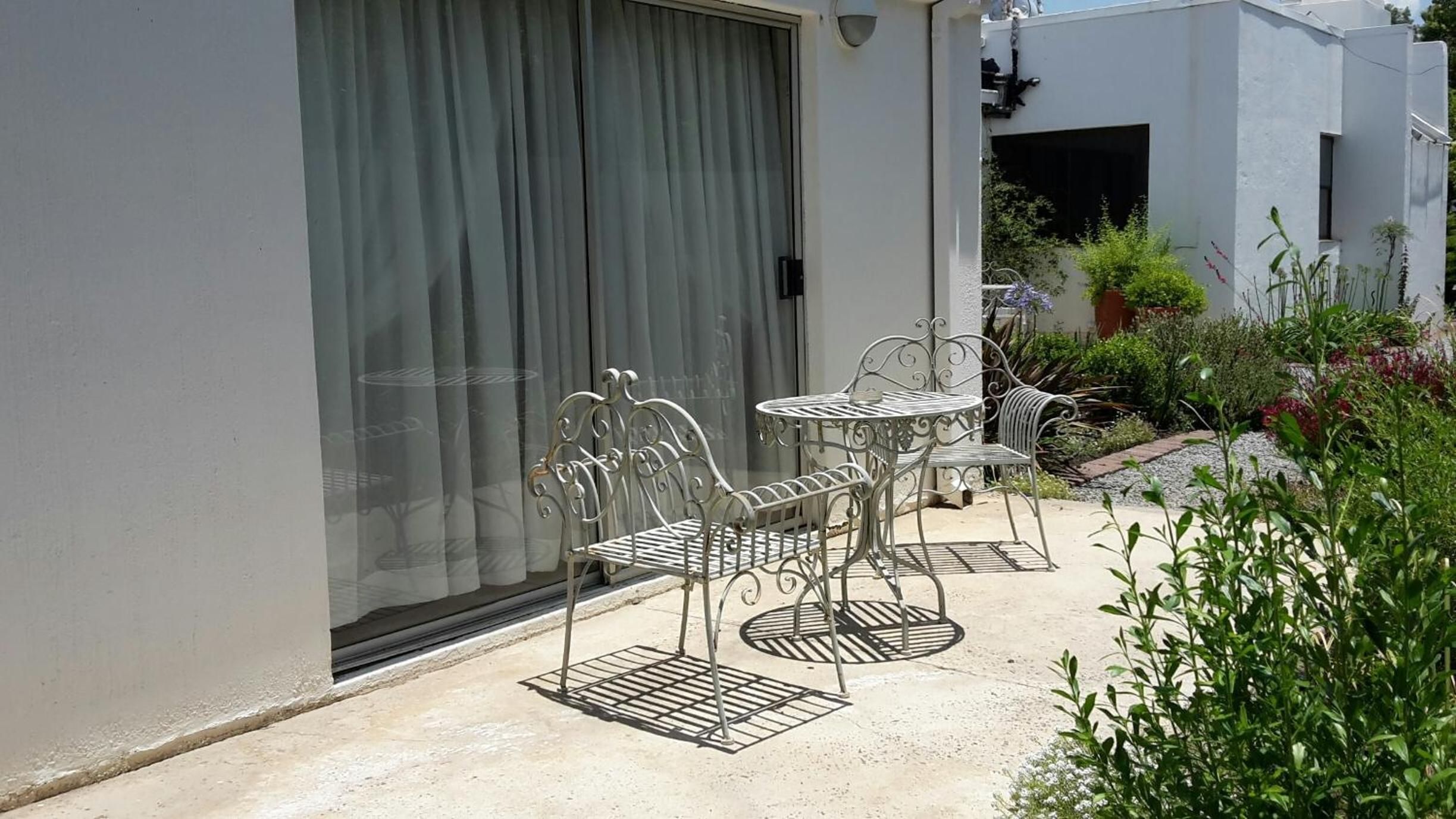 A patio with metal furniture, a sliding glass door, and a garden with various plants.
