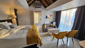 A hotel room with a bed, a desk, a chair, a small table, a shower area, and a large window with curtains.