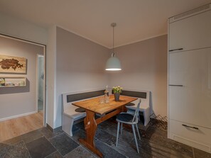 Ein Essbereich mit Holztisch, Sitzbänken, einer Hängeleuchte und einem an der Wand befestigten Regal mit Gegenständen.