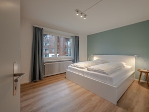 Een moderne slaapkamer met een groot bed, een raam met gordijnen, een radiator en een bedlamp.