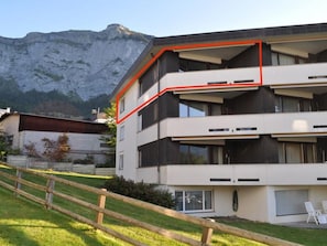 Ein modernes, zweistöckiges Gebäude mit einem Balkon, einem Holzzaun und einem Berg im Hintergrund.