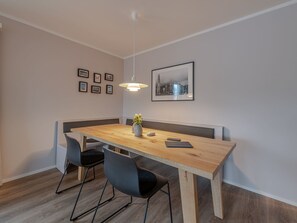 Een moderne eetruimte met een houten tafel, zwarte stoelen, een bank en een hanglamp.