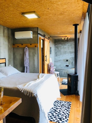 Ein Schlafzimmer mit einem Bett, einer Holzbalkendecke, einer Wand-Klimaanlage, einem kleinen Tisch mit einem Glas und einem karierten Teppich.