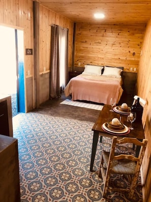 Una habitación con una cama, una mesa de comedor con sillas y un piso con diseño.