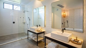 Een moderne badkamer met twee wastafels, een douche met glazen wand en een grote spiegel.