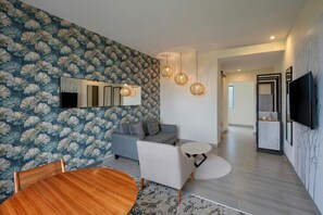 Una sala de estar moderna con un sofá, sillones, una mesa redonda de madera y un televisor montado en la pared.
