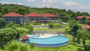 A resort with a large swimming pool, multiple buildings with red roofs, and lush greenery surrounding the property. - Aurika, Coorg - Luxury by Lemon Tree Hotels (Madikeri)