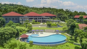Ein Resort mit großem Schwimmbecken, mehreren Gebäuden mit roten Dächern und üppiger Vegetation rund um das Anwesen.